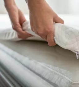 A pair of hands adjusts a thin padding on a bed. 