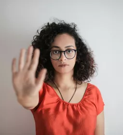 A woman with glasses stands with her arm outstretched in a "stop" gesture.