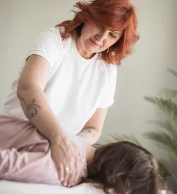 A massage therapist with red hair works on a client on a table.