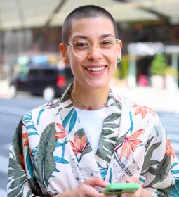 A smiling young adult stands on a street corner.