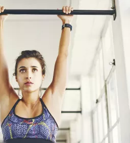 A woman hangs from a chin-up bar.