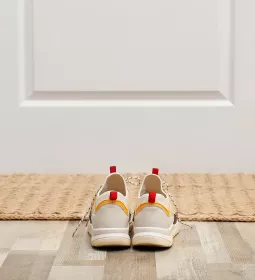 A pair of shoes sits in front of a door and welcome mat.