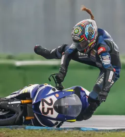 A motorcycle racer lays the bike over too far and is in midair after jumping off it.