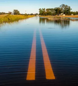 A two-lane road and surrounding fields are flooded with water.