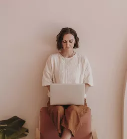 A woman sits on a chair while working on her laptop. 