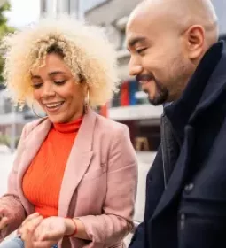 A woman shows a man her cell phone while standing outside.