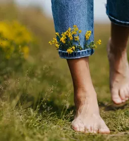 A pair of feet walk through a field with little flowers tucked into the cuff of their jeans.