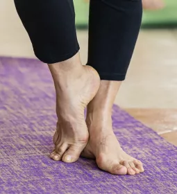 A pair of elderly feet stand on a yoga mat, one foot resting against the other.