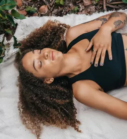 A woman lies on a blanket on the ground and practices breathwork.