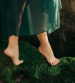 A dancer on their toes walks on a mossy bed.