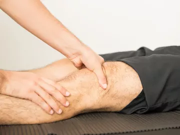 A massage therapist works on a client's knee area.