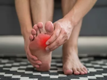 A person massages their own foot, which appears to be in pain via red coloring near their big toe. 