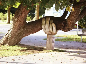 A statue of an arm and hand hold up a large branch of a tree.