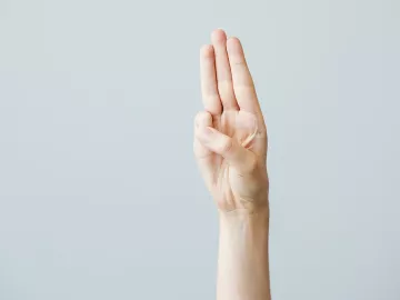 A hand displays the middle three fingers in a Scout's Honor pose with thumb and pinky finger touching.