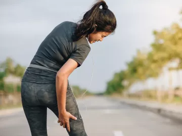 A woman grabs the back of her right leg which is causing her pain.