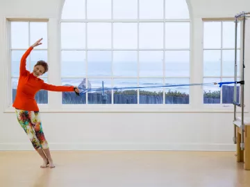 Judith Aston in a red top stretches in a dancing motion.