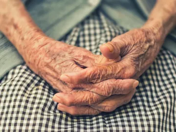 elderly woman sitting with hands folded in lap.