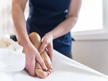 Massage therapist massaging bottom of client's foot.