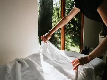 A massage therapist puts sheets on a massage table.