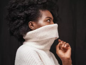 Black woman with a large knitted sweater pulled up over her face. 