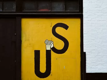 Grafitti art on an orange wall with the letters U and S spelling Us, holding hands.