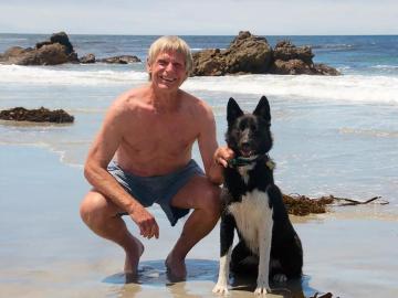 Art Riggs on Carmel Beach in Monterey County, California, smiling with his dog.