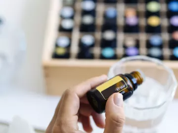 a large selection of small bottles of essential oils, with one being added to a cup.