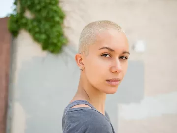 woman with bleached hair and buzzcut looks seriously towards the camera.