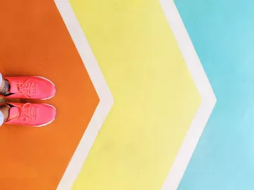 A pair of feet in pink sneakers stand on a colored path of chevron arrows.