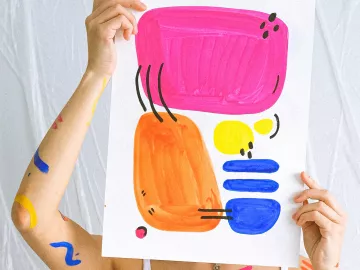 Person holding up a sheet of paper with abstract art in front of their face.
