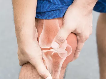 Person in shorts clutching their knee with a see-through overlay of the leg bones and joints underneath.