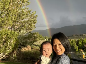 Kei Yumoto and child standing outside with a rainbow in the background.
