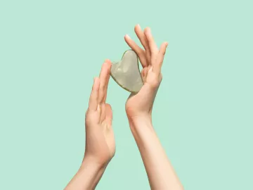 A pair of hands hold a heart-shaped rock.