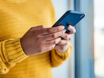A person in a yellow sweater holding their smartphone with both hands.