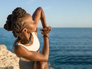 A woman twists and stretches on a cliff near the sea.