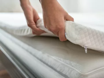 A pair of hands adjusts a thin padding on a bed. 