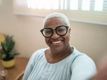 A seated woman with glasses smiling at the camera.