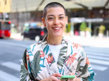A smiling young adult stands on a street corner.