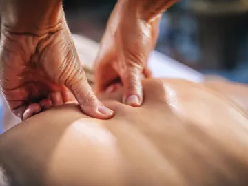 Close up image of a massage therapist's hands kneading the upper back of a client.