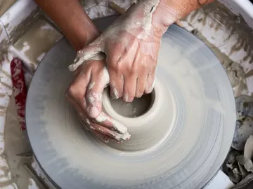 A pair of hands works on a clay pot on a pottery wheel.