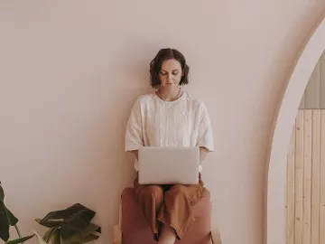 A woman sits on a chair while working on her laptop. 