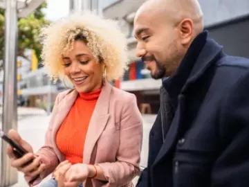 A woman shows a man her cell phone while standing outside.