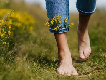 A pair of feet walk through a field with little flowers tucked into the cuff of their jeans.
