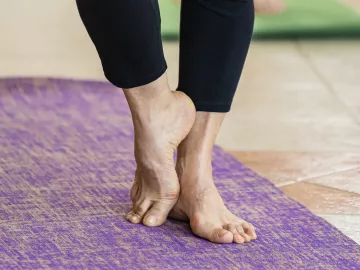 A pair of elderly feet stand on a yoga mat, one foot resting against the other.