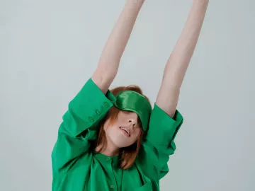 A woman wearing an eye mask stretches her arms upward.