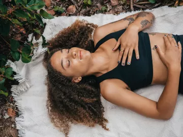 A woman lies on a blanket on the ground and practices breathwork.
