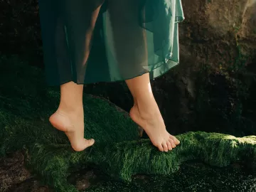 A dancer on their toes walks on a mossy bed.