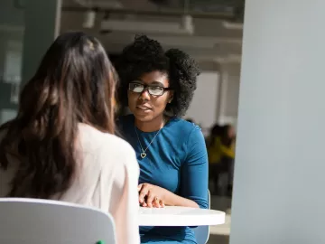 Two women at a table are seated talking.