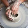 A pair of hands works on a clay pot on a pottery wheel.