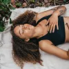 A woman lies on a blanket on the ground and practices breathwork.